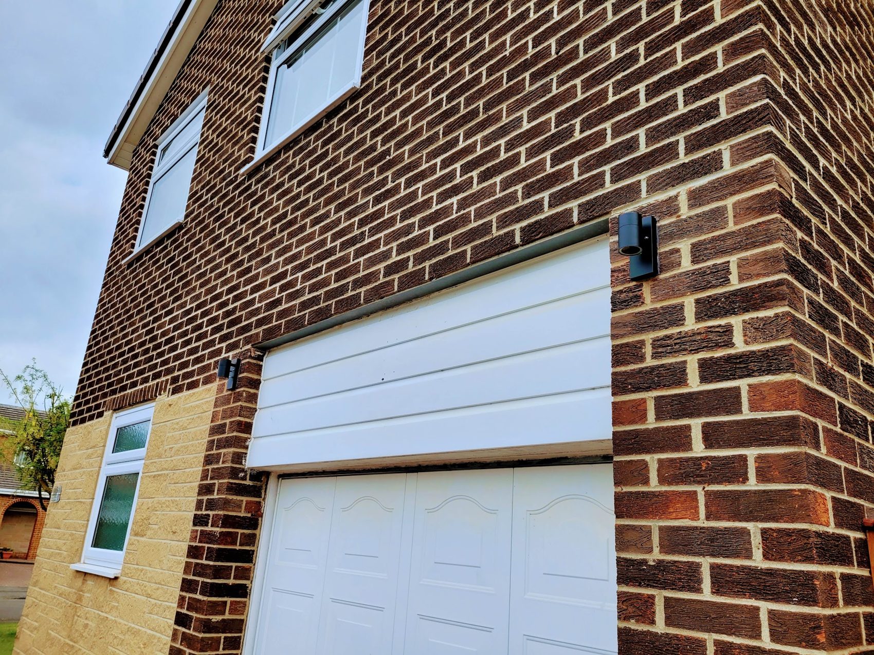 A brick house with a garage door and tidy outdoor lighting