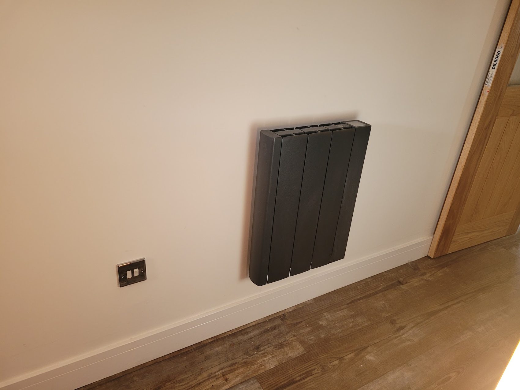 A black designer radiator fitted on a wall beside a doorway