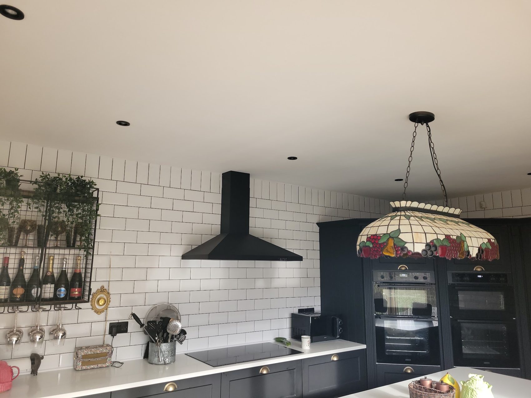 A kitchen with white metro tiles, an extractor hood and a Tiffany style pendant light